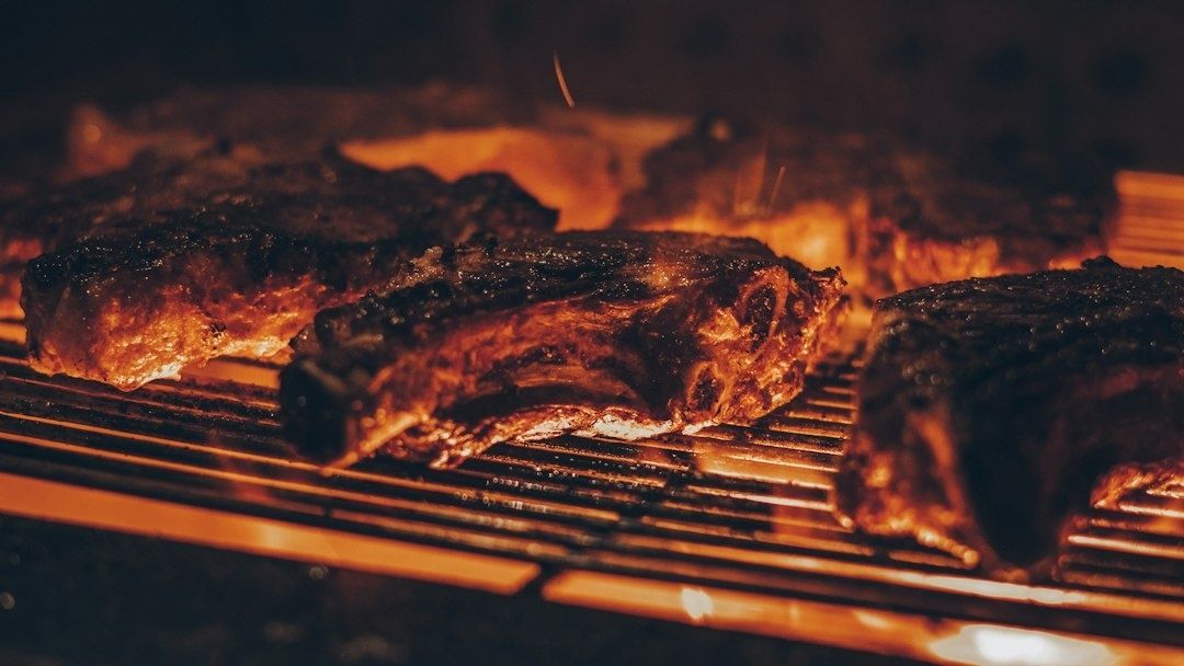 Flere mørkt grillede kødstykker på en varm rist over flammer